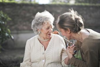 Joyful interaction between an elderly woman and her granddaughter in a sunny outdoor setting.