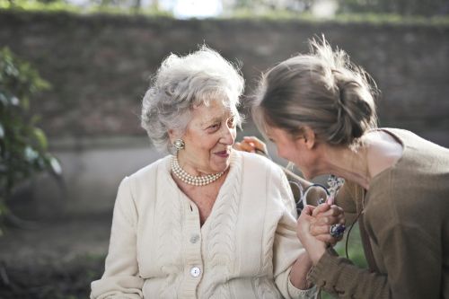 Joyful interaction between an elderly woman and her granddaughter in a sunny outdoor setting.